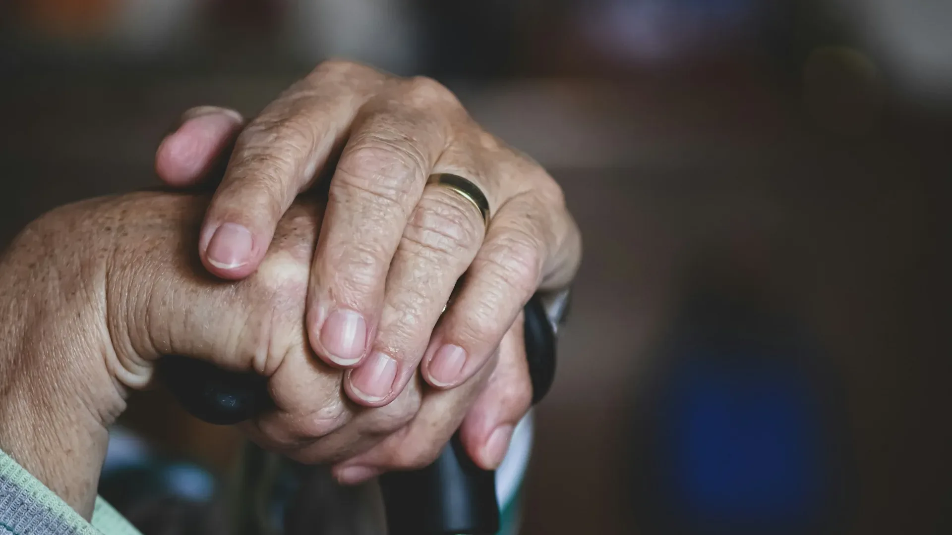 A close-up of an elderly person's hands resting on a wooden cane