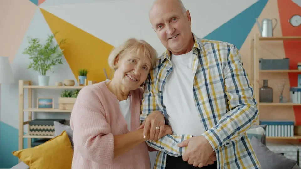 An elderly couple smiles together in a bright, colorful living room
